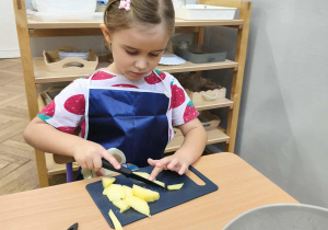 Na zdjęciu widzimy dziewczynkę, która kroi nożem ziemniaka.