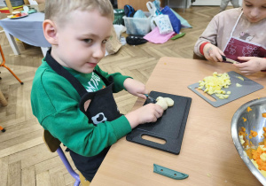 Na zdjęciu widzimy chłopca, który na desce kroi pietruszkę.