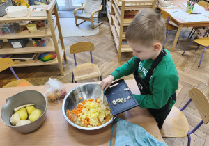 Na zdjęciu widzimy chłopca, który zsuwa pokrojoną pietruszkę do dużej miski.