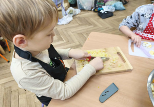 Na zdjęciu widzimy chłopca, który kroi ziemniaka.