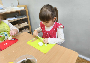 Na zdjęciu widzimy dziewczynkę, która kroi jajko do sałatki jarzynowej.