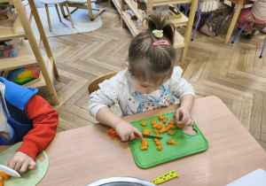 Na zdjęciu widzimy dziewczynkę, która kroi nożem marchewkę do sałatki jarzynowej.