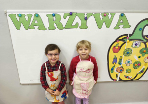 Na zdjęciu widzimy dzieci w kolorowych fartuszkach.