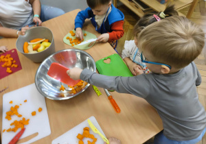 Na zdjęciu widzimy chłopca, który zsywa do dużej miski pokrojoną marchewkę.