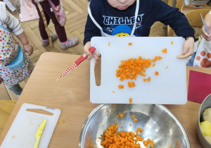 Na zdjęciu widzimy chłopca, który zsuwa z deski pokrojoną marchewkę do wspólnej miski.