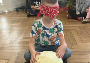 Zdjęcie przedstawia chłopca, który próbuje rozpoznać kapustę po dotyku, z zasłoniętymi oczami.