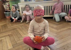 Zdjęcie przedstawia dziewczynkę, która próbuje rozpoznać paprykę po dotyku, z zasłoniętymi oczami.