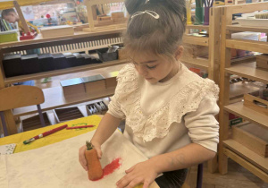 Zdjęcie przedstawia dziewczynkę stemplującą marchewką swoją torbę.