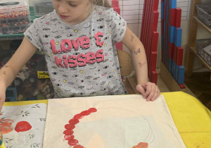 Zdjęcie przedstawia dziewczynkę stemplującą marchewką swoją torbę.