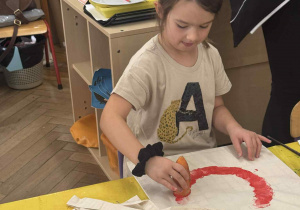 Zdjęcie przedstawia dziewczynkę stemplującą marchewką swoją torbę.