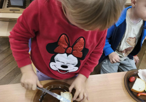 Na zdjęciu widzimy dziewczynkę, która samodzilnie smaruje sobie chleb masłem.