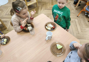 Na zdjęciu widzimy grupkę dzieci, które mają przygotowane śniadanie i czekają na "Smacznego".