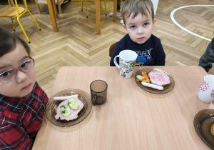 Na zdjęciu widzimy grupkę dzieci, które mają przygotowane śniadanie i czekają na "Smacznego".