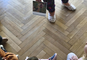 Na zdjęciu widzimy Panią, która pokazuje dzieciom zdjęcie przedstawiające psa ratownika - poszukiwacza.