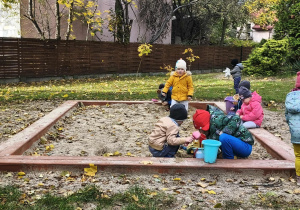 Na zdjęciu widzimy grupkę dzieci bawiącą się w piaskownicy.