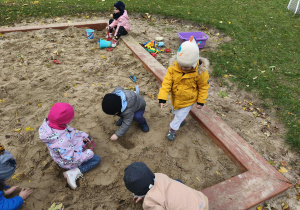 Na zdjęciu widzimy dzieci, które bawią się w piaskownicy przedszkolnej.