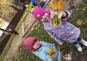 Na zdjęciu widzimy dwie dziewczynki, które trzymają w rękach kolorowe liście.