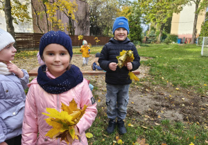 Na zdjęciu widzimy dziewczynkę i chłopca, którzy trzymają liście w rękach.
