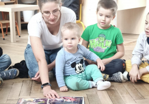 Mama czytająca książkę przedszkolakom siedzący w kole.