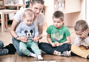 Mama czytająca książkę przedszkolakom siedzący w kole.