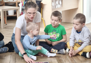 Mama czytająca książkę przedszkolakom siedzący w kole.