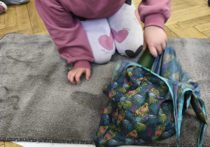 Na zdjęciu widzimy dziewczynkę, która wyjmuje coś z kolorowej torby.