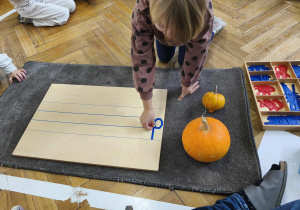 Na zdjęciu widzimy dziewczynkę, która kładzie literkę "d" na liniaturze. Dziewczynka wykorzystuje litery z ruchomego alfabetu.