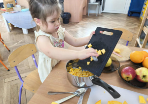 Na zdjęciu widzimy dziewczynkę, która zsuwa pokrojoną dynię do garnka.