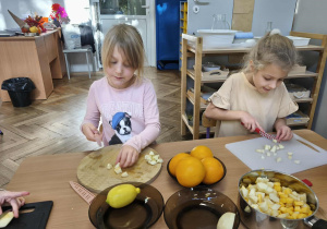 Na zdjęciu widzimy dziewczynki, które kroją kawałki jabłka.