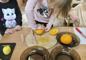 Na zdjęciu widzimy dziewczynkę, która wyciska pomarańczę.