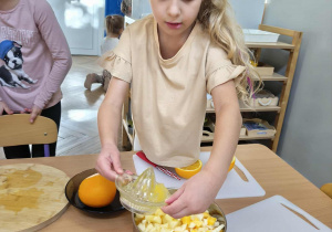 Na zdjęciu widzimy dziewczynkę, która wlewa wyciśnięty sok do garnka z dynią i jabłkiem.