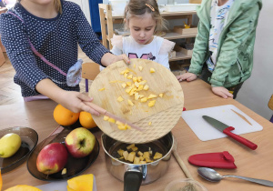 Na zdjęciu widzimy dziewczynkę, która zsuwa kawałki pokrojonej dyni do garnka.