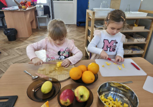 Na zdjęciu widzimy dwie dziewczynki, które kroją dynię na deskach.