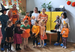 Na zdjęciu widzimy dziewczynkę, która trzyma dyniowe wiaderko. Dziewczynka uczestniczy w zabawie "Cukierek albo psikus".