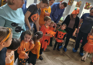 Na zdjęciu widzimy chłopca, który trzyma dyniowe wiaderko. Chłopiec uczestniczy w zabawie "Cukierek albo psikus".