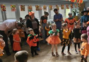 Na zdjęciu widzimy grupkę dzieci oraz rodzica, który pokazuje figurę do wykonania.