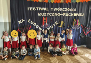 Na zdjęciu widzimy grupkę dzieci, które brały udział w Festiwalu muzyczno-ruchowym "Na ludową nutę". Dzieci które przed nimi siedzą występowały w roli obserwatorów.