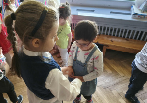 Na zdjęciu widzimy grupkę dzieci uczestniczących w tańczach i zabawach do muzyki ludowej.