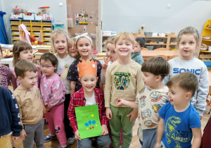 Zdjęcie grupy dzieci i jubilata, który trzyma książeczkę z laurek.