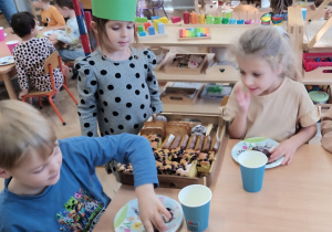 Dziewczynka częstuje dzieci ciastem.