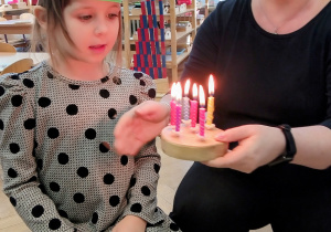 Dziewczynka zdmuchuje świeczki na symbolicznym torcie.