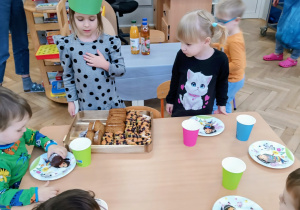 Dziewczynka częstuje dzieci ciastem.