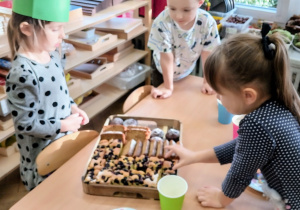 Dziewczynka częstuje dzieci ciastem.