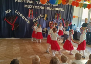 Zdjęcie przedstawia dzieci ubrane w stroje biało- czerwone. Dzieci prezentują taniec ludowy.
