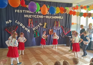 Zdjęcie przedstawia dzieci ubrane w stroje biało- czerwone. Dzieci prezentują taniec ludowy.