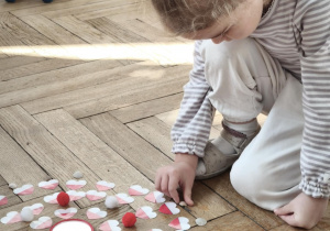 Dziecko układa mandalę składająca sie z biało czerwonych serc i muszelek