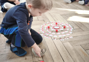 Dziecko układa mandalę składająca sie z biało czerwonych serc i muszelek