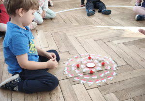 Dziecko układa mandalę składająca sie z biało czerwonych serc i muszelek