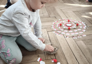 Dziecko układa mandalę składająca sie z biało czerwonych serc i muszelek