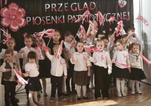 Dzieci śpiewają piosenkę patriotyczną i machają wstęgami biało - czerwonymi